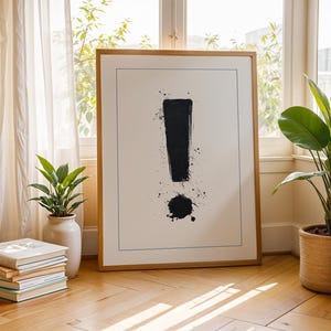Könnte beinhalten: Ein gerahmter Schwarzweißdruck eines Ausrufezeichens mit schwarzen Farbstichen auf weißem Hintergrund. Der Rahmen ist aus Holz und hat eine natürliche Oberfläche.