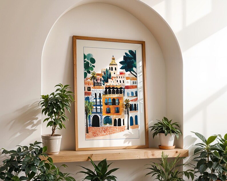 May include: A framed watercolour painting of a colourful cityscape with buildings, trees, and a church steeple. The painting is in a light wood frame and is hanging on a wall.