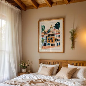 May include: A bedroom with a white bed with a wooden headboard and a white duvet. There are two beige pillows on the bed. A framed print of a colourful cityscape hangs on the wall above the bed. A white sheer curtain hangs in the window to the left of the bed.