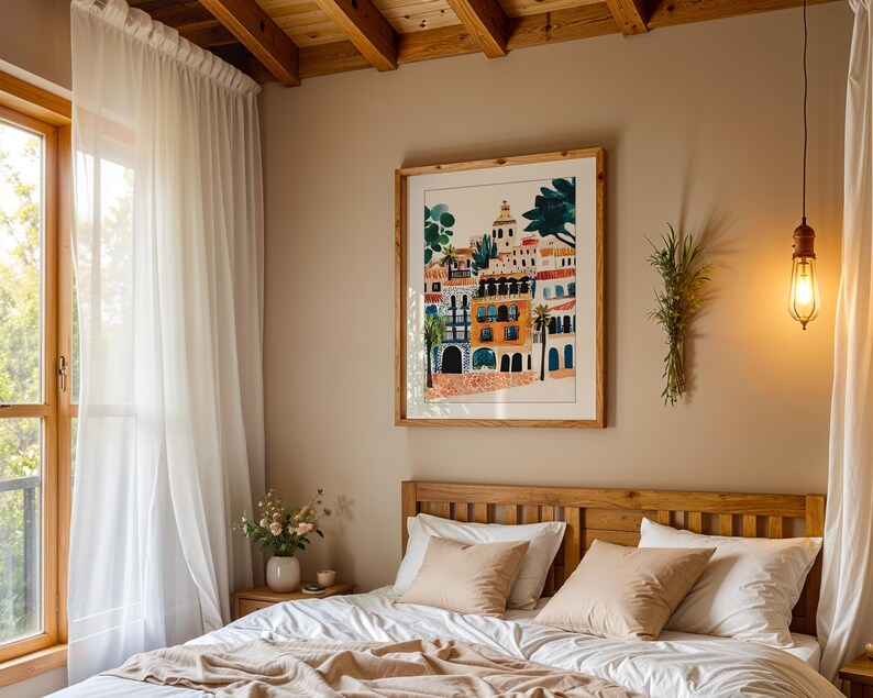 May include: A bedroom with a white bed with a wooden headboard and a white duvet. There are two beige pillows on the bed. A framed print of a colourful cityscape hangs on the wall above the bed. A white sheer curtain hangs in the window to the left of the bed.