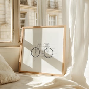 Puede incluir: Un dibujo en blanco y negro de una bicicleta con una cesta en el manillar, enmarcado. El marco es de madera clara y el dibujo está sobre un fondo blanco.