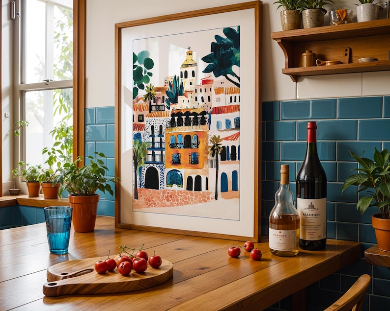 May include: A framed illustration of a colourful cityscape with buildings, palm trees, and a church steeple. The illustration is on a white background and is framed in a natural wood frame. The frame is sitting on a wooden table with a glass of water, a chopping board with cherries, and two bottles of wine.