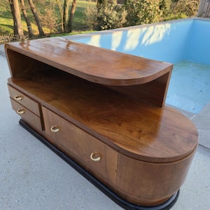 May include: A mid-century modern wooden cabinet with a curved top and drawers. The cabinet is made of a rich, dark wood with a glossy finish. It has gold-colored handles and a black base. The cabinet is approximately 60 inches long.