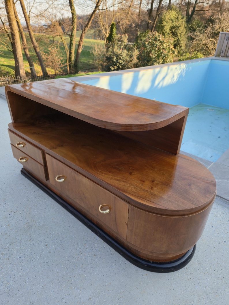 May include: A mid-century modern wooden cabinet with a curved top and drawers. The cabinet is made of a rich, dark wood with a glossy finish. It has gold-colored handles and a black base. The cabinet is approximately 60 inches long.