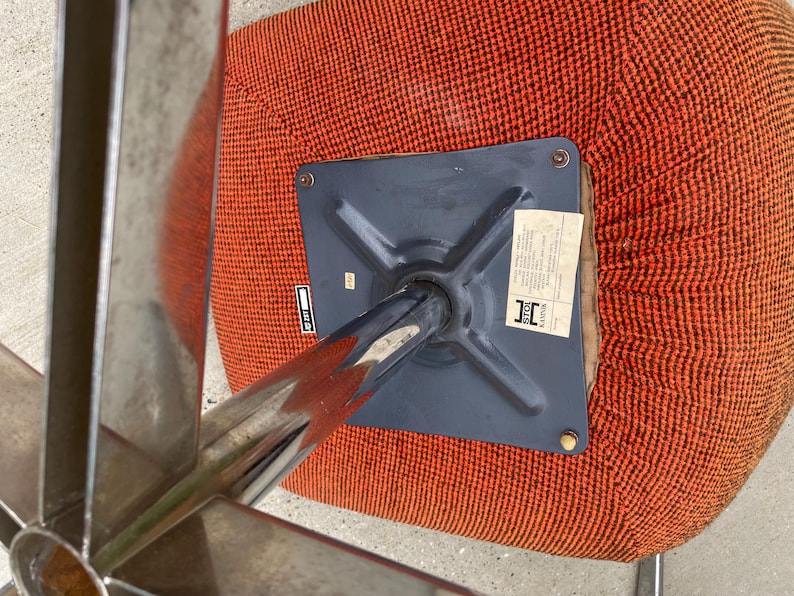 Peut inclure: Le dessous d'une chaise pivotante avec une base en m&eacute;tal noir et un si&egrave;ge en tissu rouge. La base porte une &eacute;tiquette indiquant "Fabriqu&eacute; en Chine".