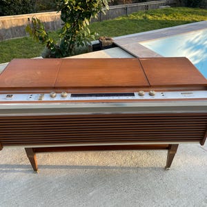 Puede incluir: Una consola estéreo vintage de madera con una placa frontal plateada y un tocadiscos. El estéreo tiene una radio incorporada y un tocadiscos. La consola está en buen estado y tiene un aspecto retro.