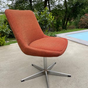 Peut inclure: Une chaise pivotante avec un si&egrave;ge en tissu rouge orang&eacute; et une base chrom&eacute;e &agrave; cinq branches.