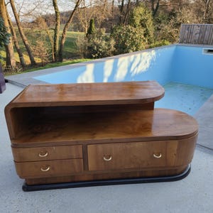 Può includere: Un mobile in legno in stile moderno della metà del secolo, con un piano curvo e tre cassetti. Il mobile è realizzato in legno dai toni caldi con finitura lucida. Ha maniglie a mezzaluna color ottone e una base nera.