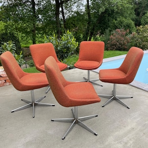 Peut inclure: Quatre chaises pivotantes avec un rev&ecirc;tement en tissu orange et des pieds chrom&eacute;s. Les chaises sont dispos&eacute;es en carr&eacute; sur une terrasse en b&eacute;ton.
