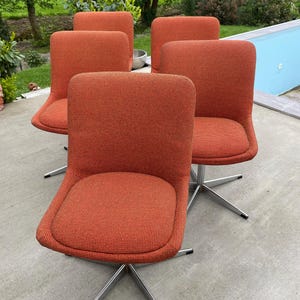 Peut inclure: Quatre chaises pivotantes orange avec des bases chrom&eacute;es. Les chaises sont dispos&eacute;es en demi-cercle sur une terrasse en b&eacute;ton.
