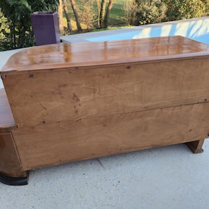 May include: A vintage wooden cabinet with a curved front and a rectangular top. The cabinet is made of light brown wood with a glossy finish. The base is a darker brown color. The cabinet is likely used for storage.