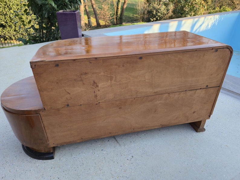 May include: A vintage wooden cabinet with a curved front and a rectangular top. The cabinet is made of light brown wood with a glossy finish. The base is a darker brown color. The cabinet is likely used for storage.
