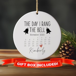 May include: White round ornament with black text that reads "The Day I Rang The Bell" with a calendar for November 2023 with the 30th circled in red. The name Kimberly is written below the calendar.