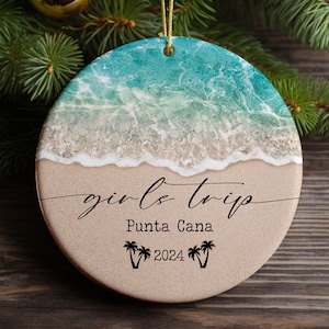 May include: Round, white, and blue Christmas ornament with a beach scene and the text "girls trip Punta Cana 2024".