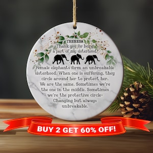 May include: A white round ornament with a marble pattern and green floral accents. The ornament features a quote about female elephants forming an unbreakable sisterhood. The text "THERESA" and "Thank you for being a part of my sisterhood." is printed on the ornament. Three black silhouette elephants are shown on the ornament. The text "BUY 2 GET 60% OFF!" is printed on a red ribbon at the bottom of the image.