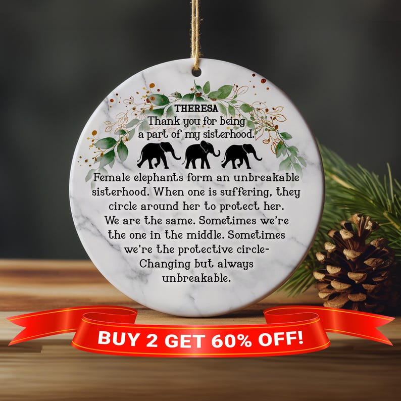 May include: A white round ornament with a marble pattern and green floral accents. The ornament features a quote about female elephants forming an unbreakable sisterhood. The text "THERESA" and "Thank you for being a part of my sisterhood." is printed on the ornament. Three black silhouette elephants are shown on the ornament. The text "BUY 2 GET 60% OFF!" is printed on a red ribbon at the bottom of the image.
