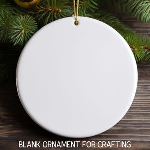 May include: A white ceramic round ornament with a gold string attached. The ornament is blank and ready for crafting.