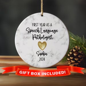 May include: White marble-patterned Christmas ornament with a gold heart and the text "First Year as a Speech Language Pathologist" with the name "Sophia" and the year "2024" below the heart.  Gift box included.