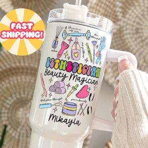 May include: White tumbler with a handle, decorated with colorful illustrations of beauty tools and the words "Esthetician Beauty Magician" and "Mikayla". The tumbler also has the text "Skincare is self care" and "no filters".