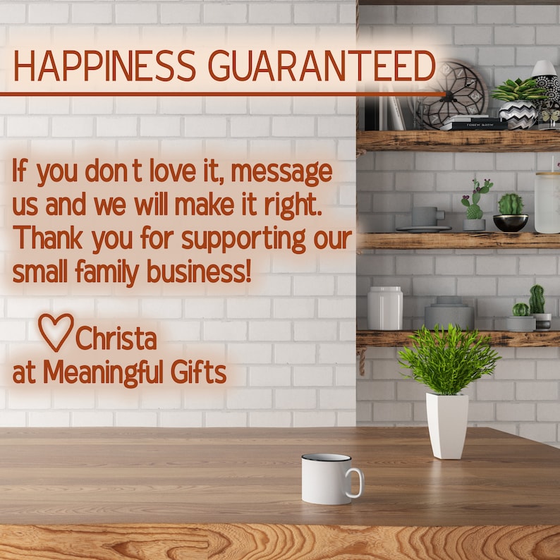 May include: A white ceramic mug with a black rim sits on a wooden surface. The background features a white brick wall with wooden shelves and greenery. The text "HAPPINESS GUARANTEED" is displayed in orange at the top of the image. The text "If you don't love it, message us and we will make it right. Thank you for supporting our small family business! Christa at Meaningful Gifts" is also displayed in orange.