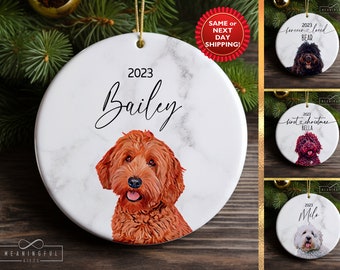 May include: A white ceramic Christmas ornament with a marble pattern featuring a brown and white dog with the text "2023 Bailey" on the ornament.