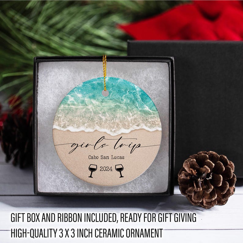 May include: A round ceramic ornament with a beach scene and the text "girls trip Cabo San Lucas 2024". The ornament is in a gift box with a ribbon.