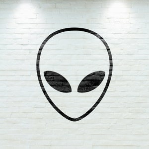 May include: A black alien head graphic on a white brick wall. The alien head is a simple outline with large, almond-shaped eyes. The brick wall has a textured surface.