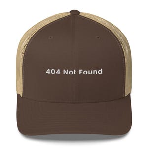 May include: A brown trucker cap with a beige mesh back. The words "404 Not Found" are embroidered in white on the front. This cap is a humorous accessory.