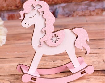 May include: A pink wooden rocking horse with a glitter finish. The horse has a white body and pink mane and tail. The rocking base is also pink.