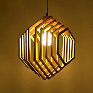May include: A wooden pendant light fixture with a hexagonal shape. The light is made of multiple layers of wood, creating a geometric pattern. The light is turned on and emits a warm glow.
