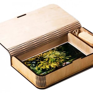 Puede incluir: Una caja de madera con tapa abatible, abierta para revelar una foto y una memoria USB de madera. La caja está hecha de madera clara con un acabado natural. La foto muestra un árbol con hojas verdes.