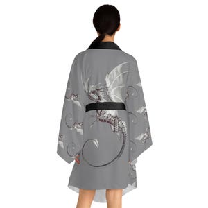 Può includere: Accappatoio grigio in stile kimono con una dettagliata illustrazione di drago, ali e accenti bianchi. L'accappatoio ha una cintura e finiture nere e un motivo ripetuto di elementi di drago.