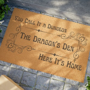 May include: A brown coir doormat with the text "You call it a dungeon, The Dragon's Den, Here it's home" in black lettering.