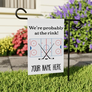 K&ouml;nnte beinhalten: Wei&szlig;e Gartenflagge mit einem Eishockeyfeld und gekreuzten Schl&auml;gern. Der Text lautet "We're probably at the rink!" und "YOUR NAME HERE".