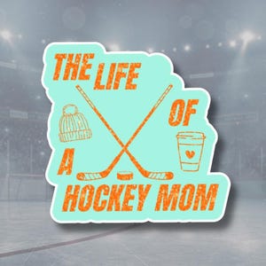 May include: A teal sticker with the text "THE LIFE OF A HOCKEY MOM" in orange, featuring crossed hockey sticks, a beanie, and a coffee cup. The sticker is set against a blurred hockey rink background.
