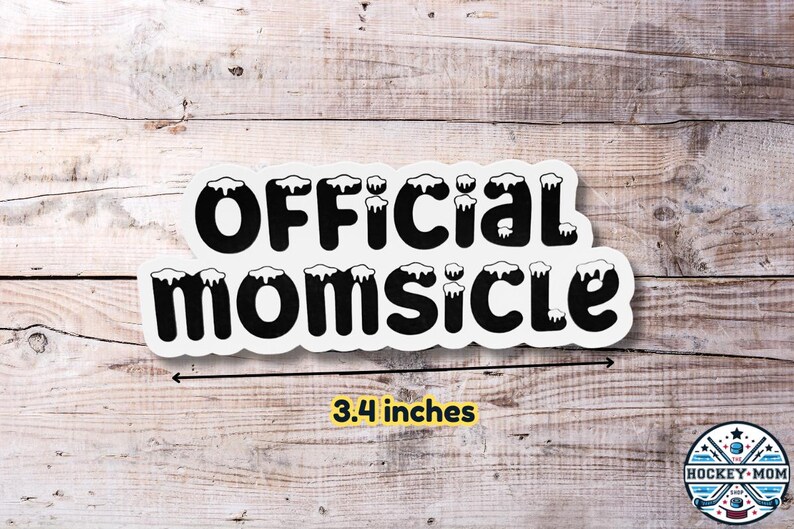 May include: White sticker with black text that reads "OFFICIAL MOMSICLE" with a white outline and a dripping effect. The sticker is 3.4 inches wide and is on a wood background.
