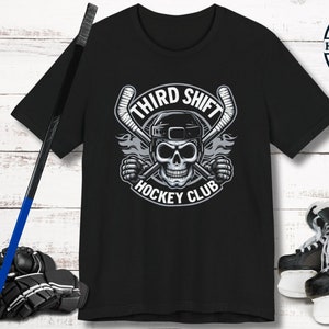May include: Black t-shirt with a graphic of a skull wearing a hockey helmet and holding two hockey sticks. The text "Third Shift Hockey Club" is printed below the skull.
