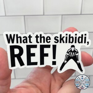 May include: A white sticker with black text that reads "What the skibidi, REF!" and a black and white illustration of a referee with a whistle.