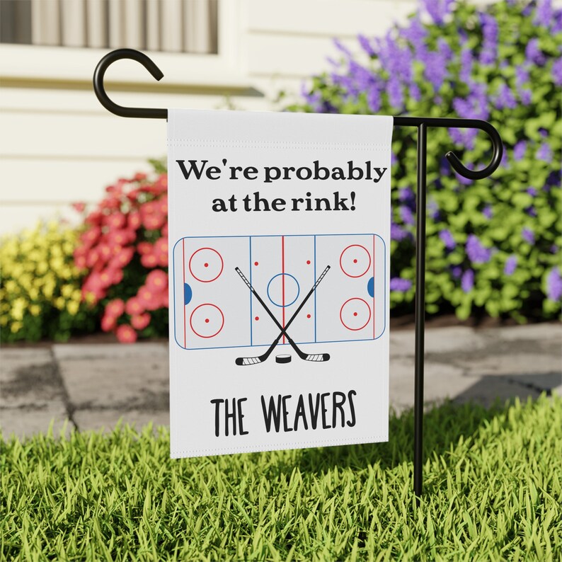 K&ouml;nnte beinhalten: Wei&szlig;e Gartenflagge mit einem Eishockeyfeld-Design und dem Text "We're probably at the rink!" und "THE WEAVERS".