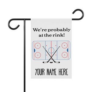 K&ouml;nnte beinhalten: Eine wei&szlig;e Gartenflagge mit einem Hockeyfeld und Schl&auml;gern, dem Text "We're probably at the rink!" und dem Text "YOUR NAME HERE".