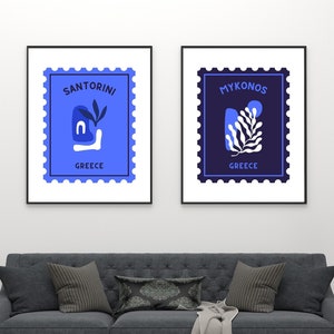 May include: Two framed prints with a blue and white stamp design. The left print says "Santorini Greece" and the right print says "Mykonos Greece".