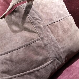 May include: A large, gray suede tote bag with a stitched design. The bag has a wide, flat handle and multiple compartments.
