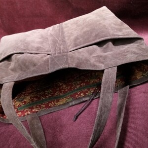 May include: A large, brown suede tote bag with a zippered pocket and a patterned fabric lining. The bag has two long straps.