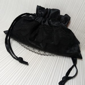 May include: A black satin drawstring bag with a lace trim. The bag is closed and the drawstring is tied in a knot.