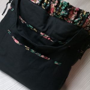 Puede incluir: Una bolsa de mano negra con forro de estampado floral. La bolsa tiene cierre de cordón y una sola correa.