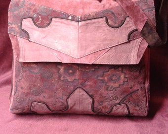 May include: A pink suede shoulder bag with a flap closure and a brown leather strap. The bag has a patchwork design with different shades of pink and brown suede and a floral pattern.