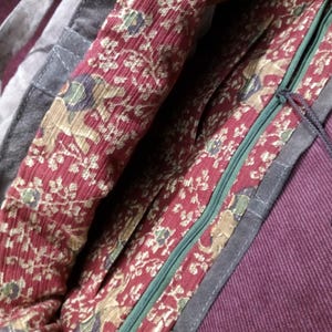 May include: A dark gray canvas tote bag with a red and gold floral print lining. The bag has a zipper closure and a long black strap.