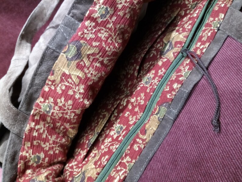 May include: A dark gray canvas tote bag with a red and gold floral print lining. The bag has a zipper closure and a long black strap.