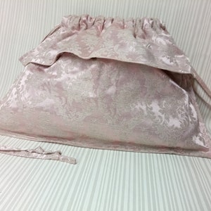 May include: A pink drawstring bag with a floral pattern. The bag is made of a soft, silky fabric and has a gathered top.
