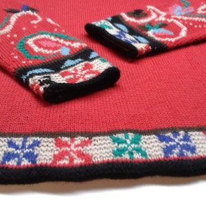 May include: Red knitted sweater with a colorful floral pattern on the sleeves and a snowflake pattern on the bottom hem.